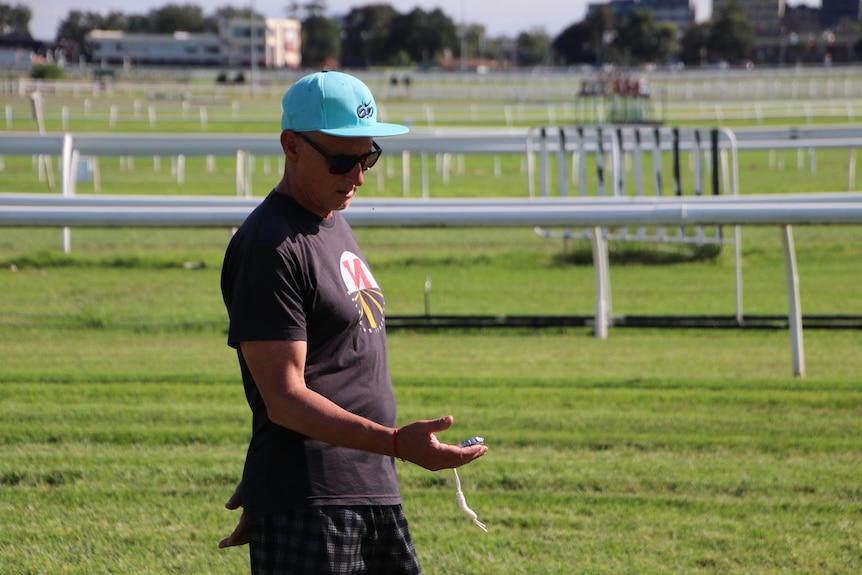 Nic Bideau stands holding a stop watch at a race course