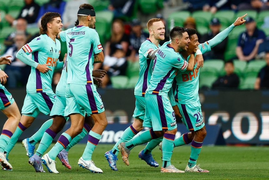 Perth Glory players celebrate a goal with one pointing into the stands.
