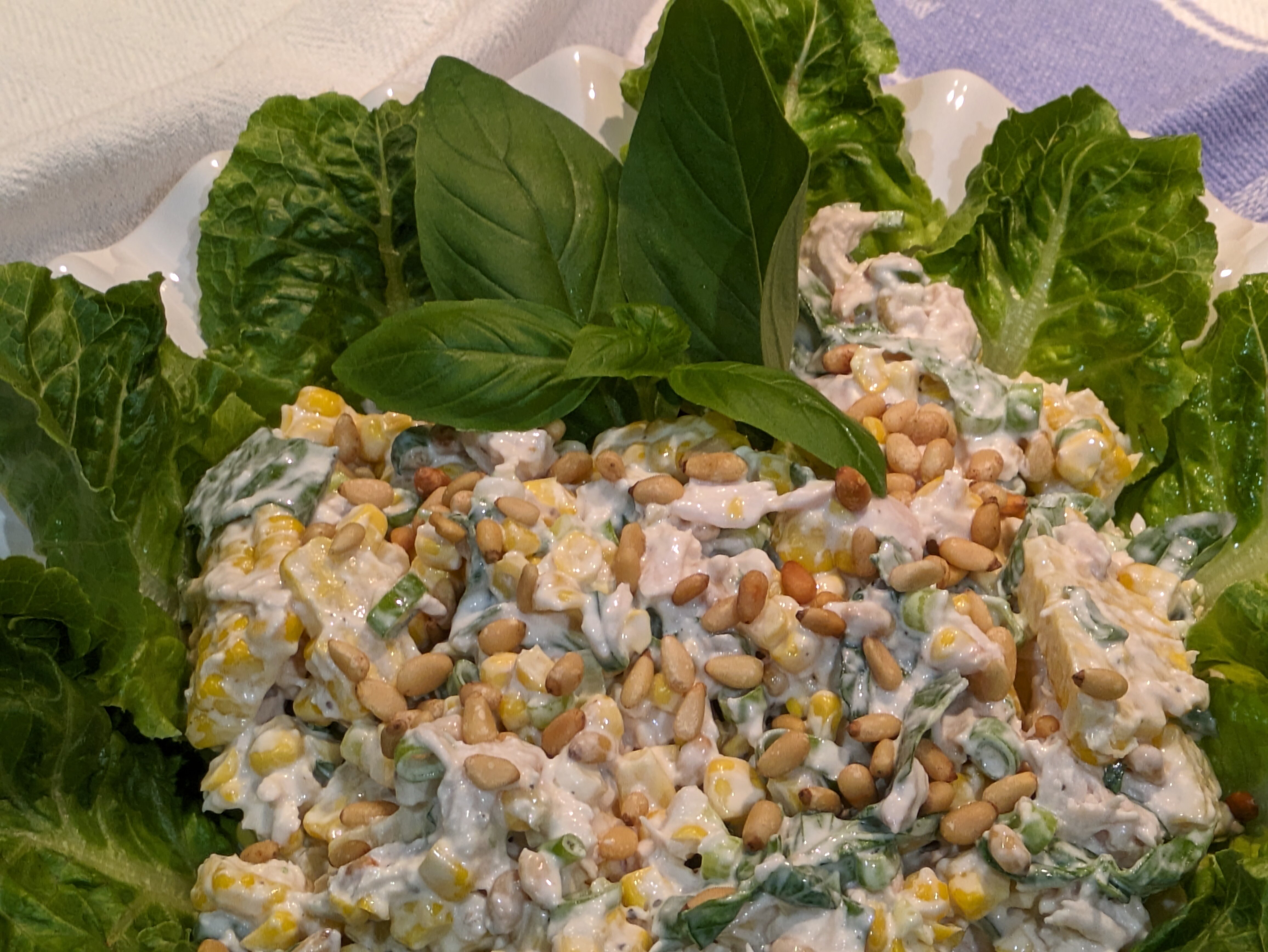 A close-up of a chicken and corn salad, sitting on top of green salad leaves.