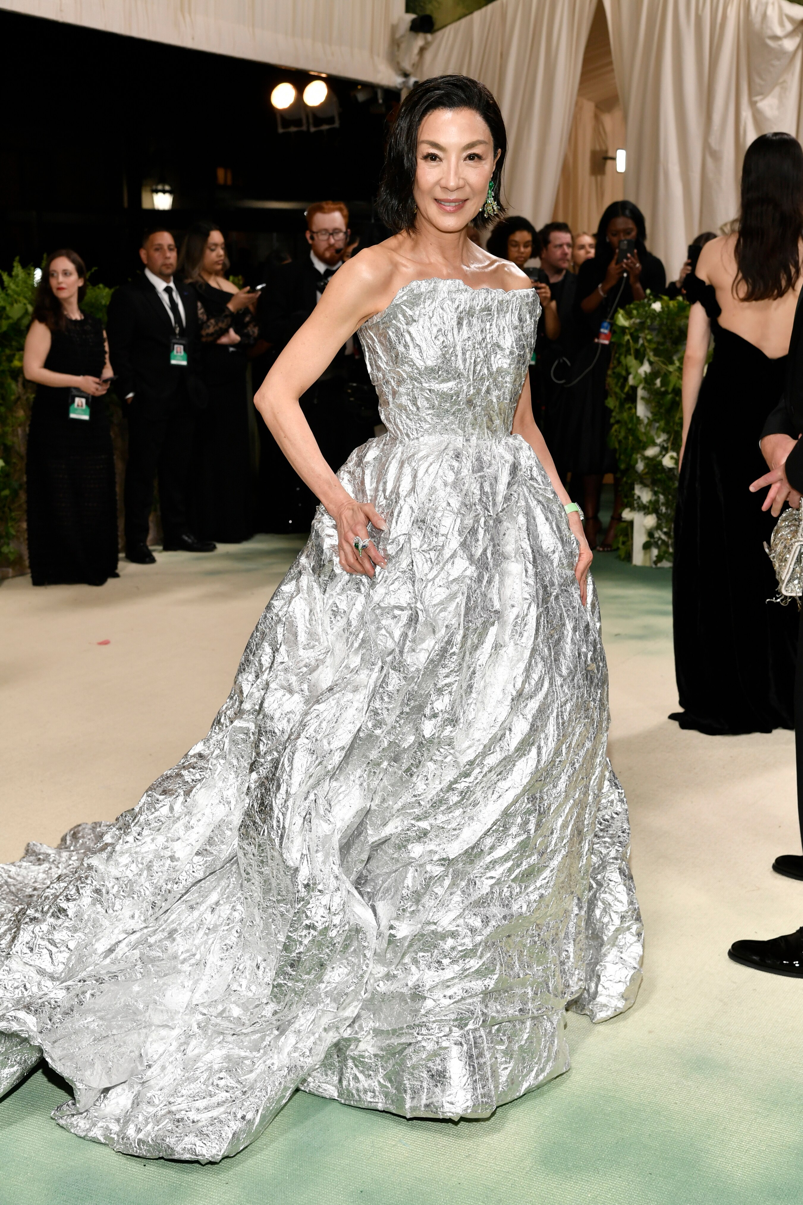 Michelle Yeoh wearing a long silvery strapless gown with a puffy skirt and a crinkly train