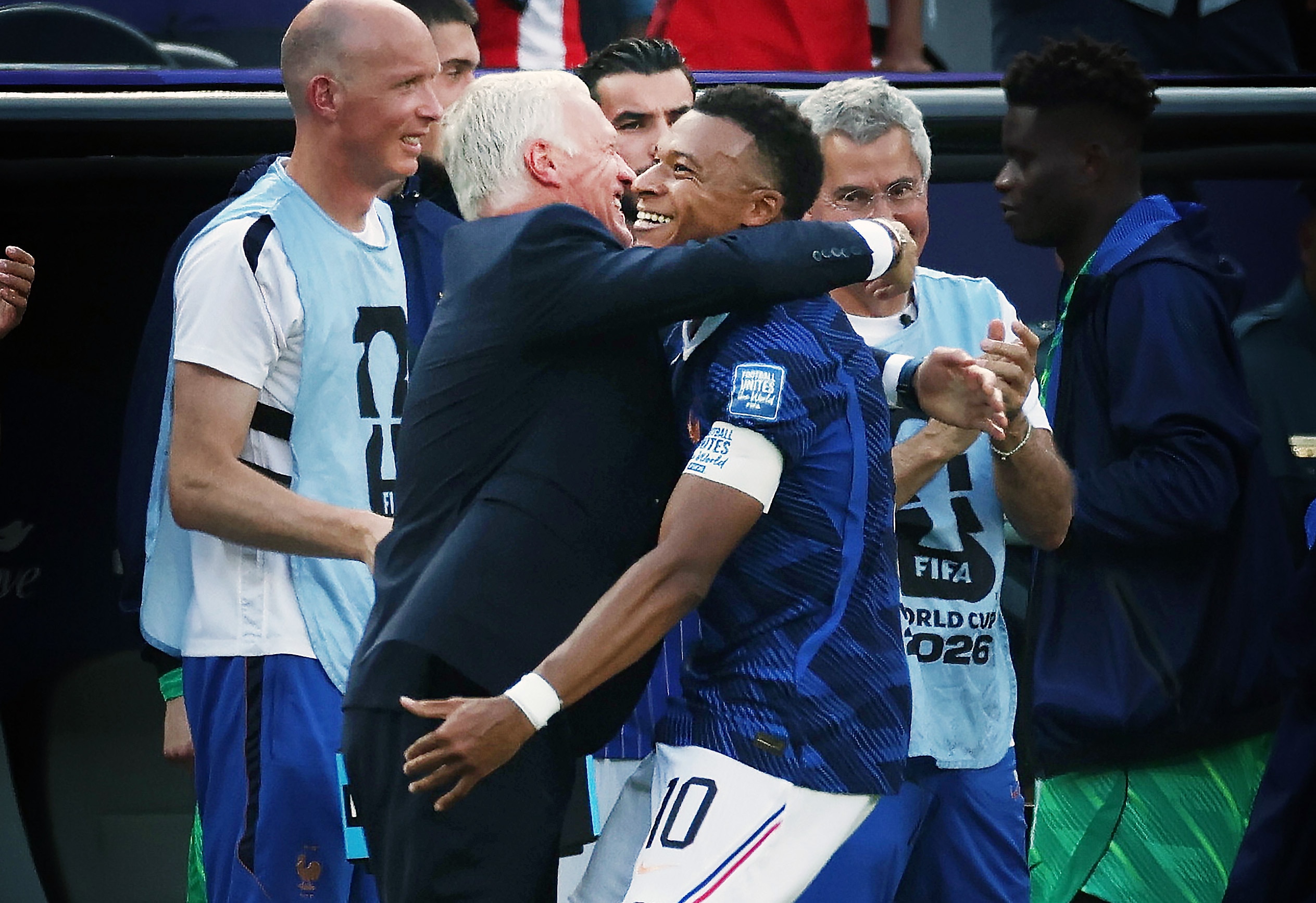Didier Deschamps and Kylian Mbappe smile and hug on the touchline
