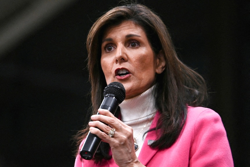 A woman in pink talks into a microphone