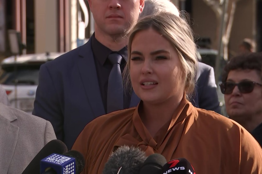 A blonde woman reads a statement to the media