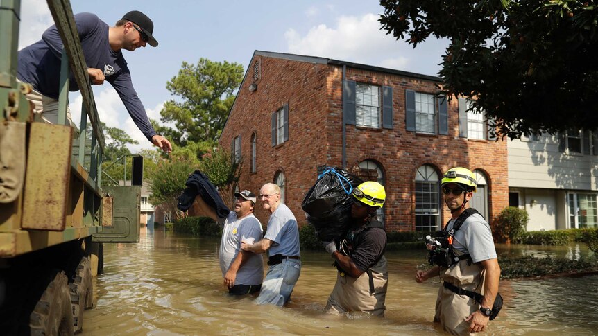 Two men and two rescue workers stand in brown flood water next to a truck as a man leans out to get their possessions.