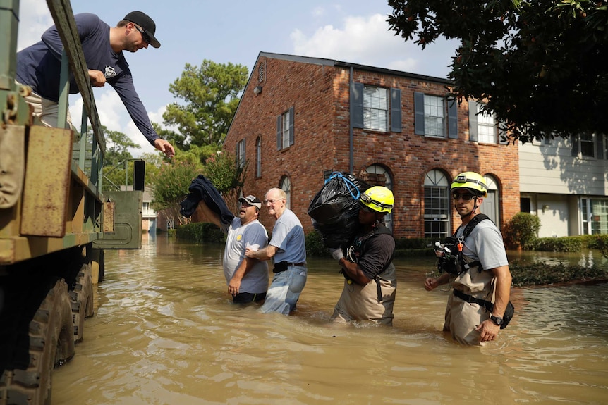 Two men and two rescue workers stand in brown flood water next to a truck as a man leans out to get their possessions.