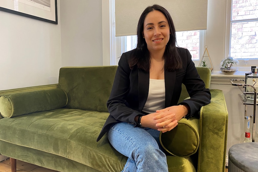 A woman wearing a white top and a black blazer sitting on a green couch.