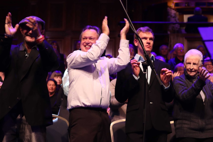 A row of people clapping and smiling on a stage