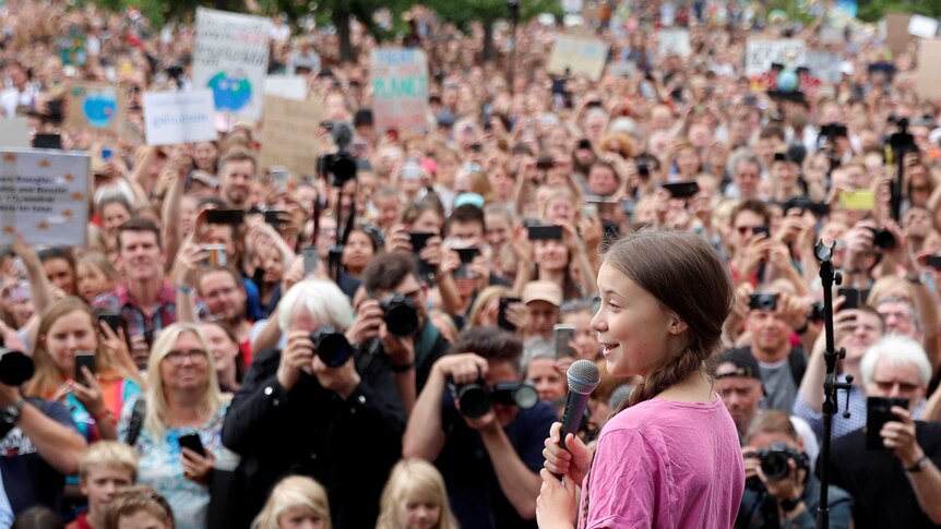 Greta Thunberg holds a microphone on stage as she speaks to a crowd