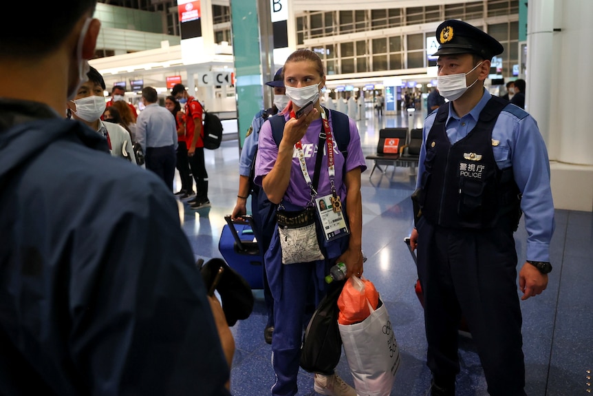 Belarusian sprinter Krystsina Tsimanouskaya stands with police at Tokyo airport, carrying her luggage. 