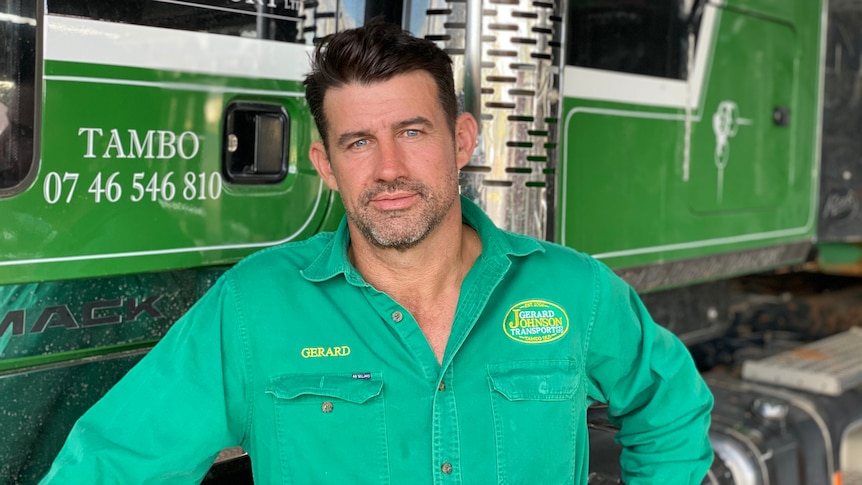 A man in a long sleeved green shirt stands in front of a cattle truck