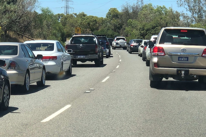 A line of cars banked up on a Perth road with trees in the background.