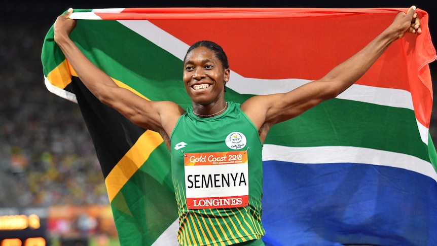 Caster Semenya holds the South African flag behind her, with arms stretched out.