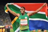 Caster Semenya holds the South African flag behind her, with arms stretched out.