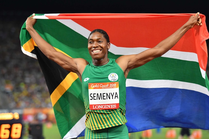 Caster Semenya holds the South African flag behind her, with arms stretched out.