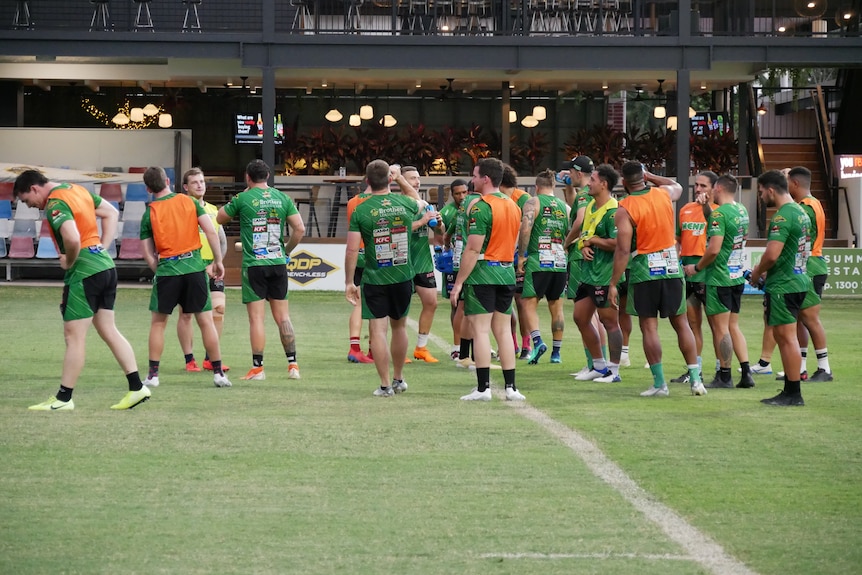 A team of footballers standing in the middle of field wearing green shirt and  orange high visibility training bibs