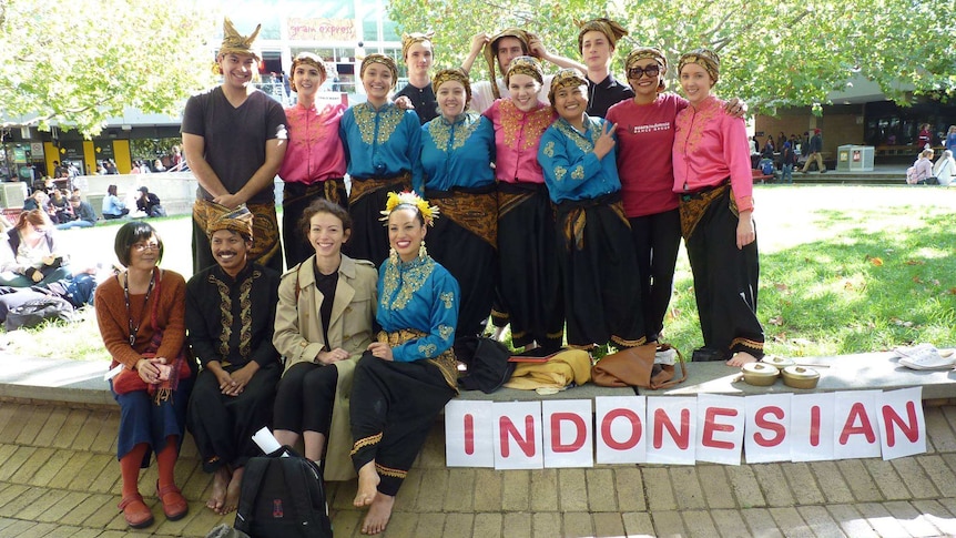 A group of people standing outside a campus with papers says Indonesian