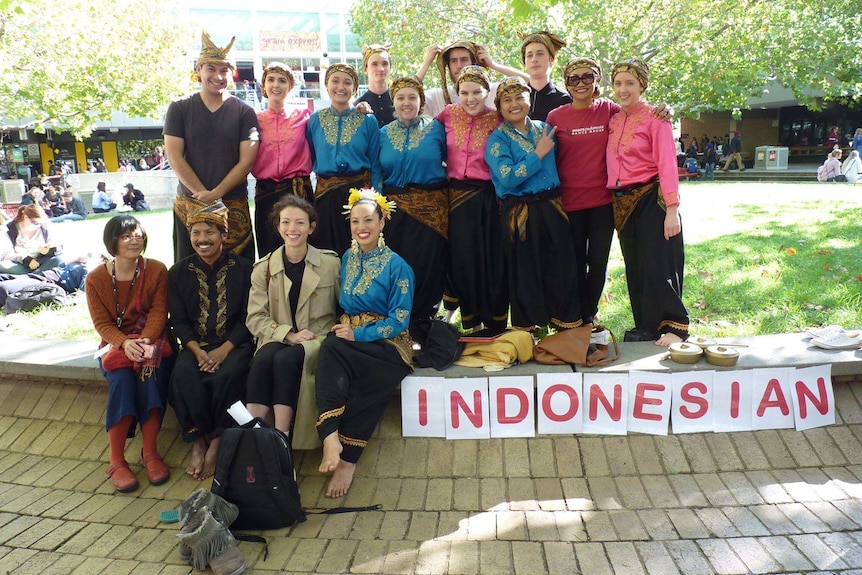 A group of people standing outside a campus with papers says Indonesian