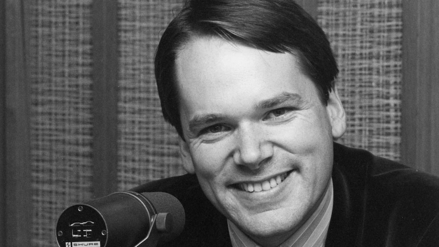 Mark Colvin smiles in front of a microphone.