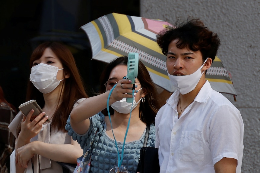 A woman uses a portable fan to cool down a man.