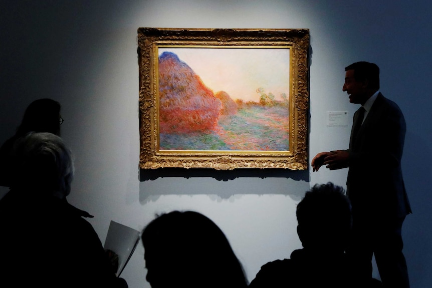 Silhouettes of people can be seen around the gold-framed impressionist painting, which hangs on a blue wall.