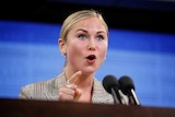 Grace Tame speaks and points at a lectern.