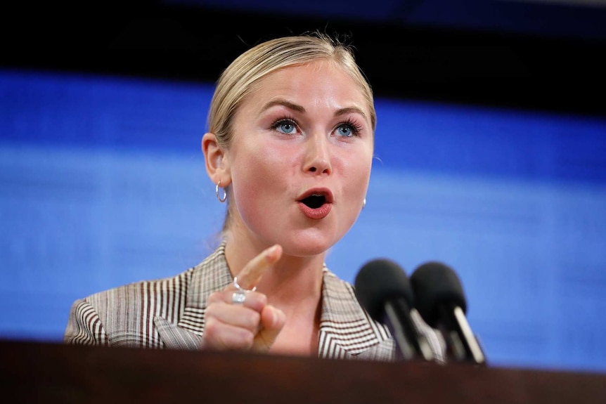 Grace Tame speaks and points at a lectern.