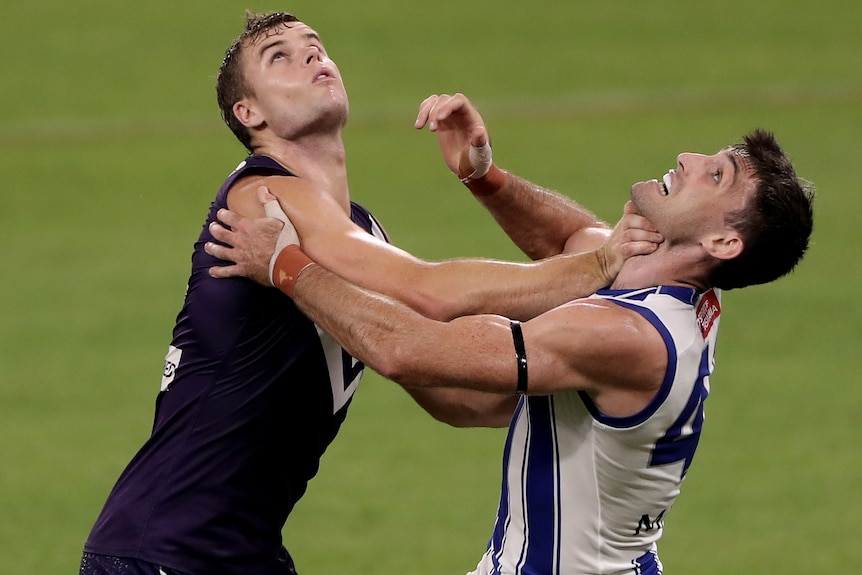 A Fremantle AFL player pushes against a North Melbourne opponent as they look to the sky.