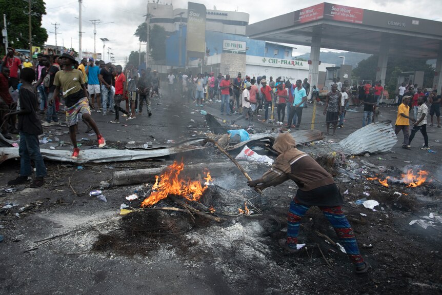 a person throws wood on a fire in the street as demonstrators stand nearby