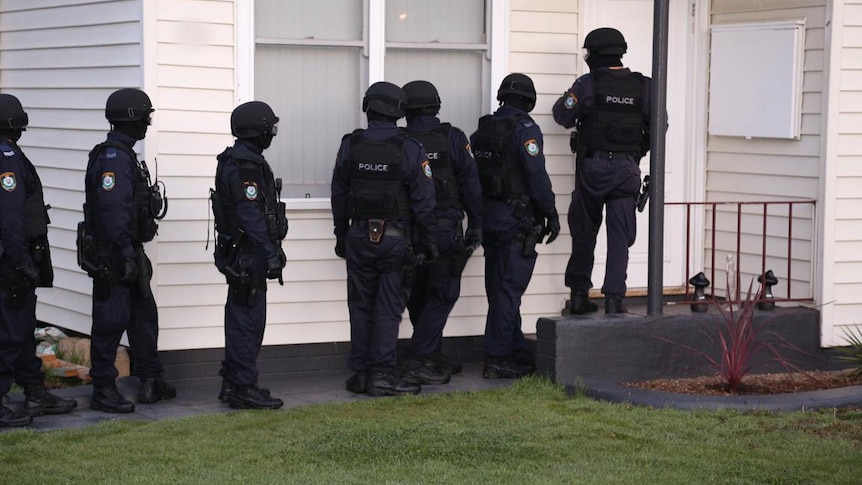 a group of seven tactical officers dressed in riot gear standing out the front of a house