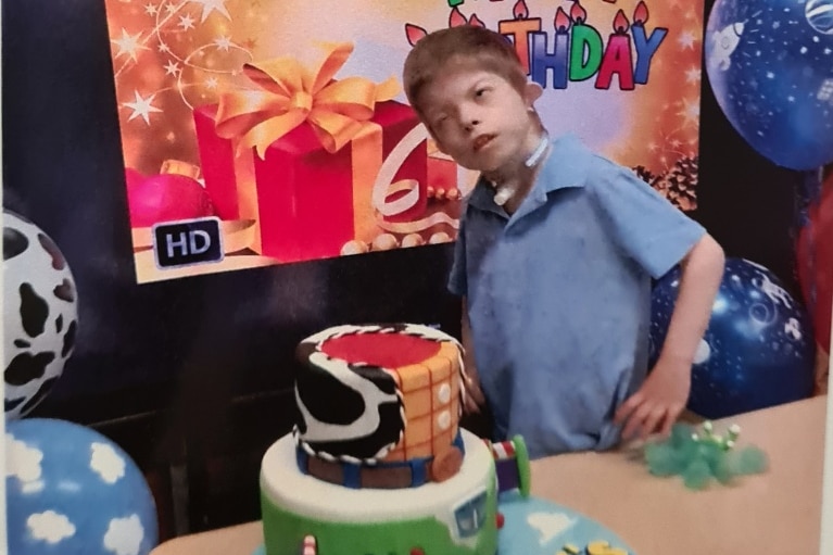 A boy in a blue shirt stands behind a large toy story themed cake.