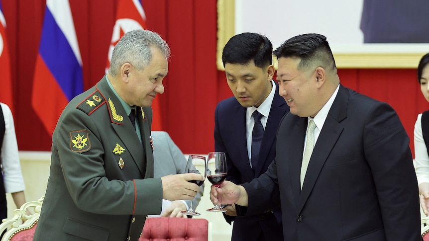 Kim Jong Un smiles as he clinks a red wine glass with a western man in military uniform in reception room