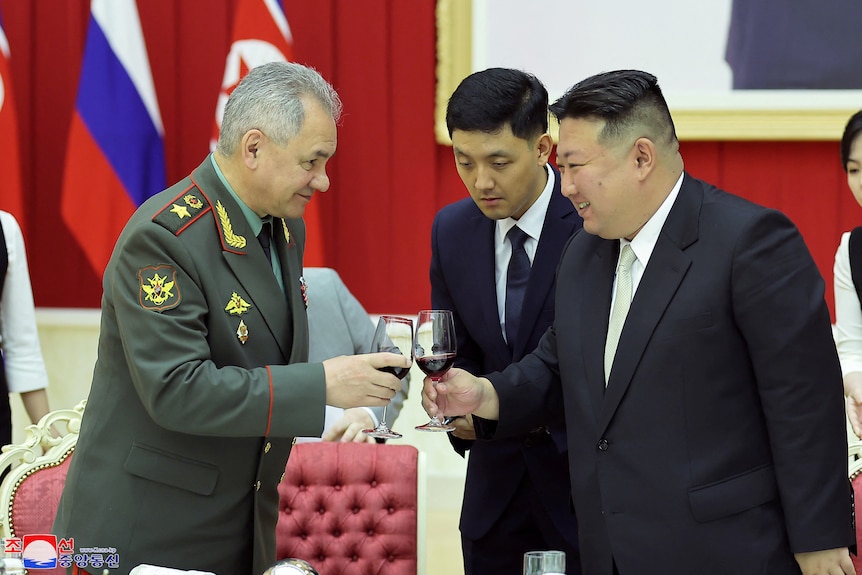 Kim Jong Un smiles as he clinks a red wine glass with a western man in military uniform in reception room