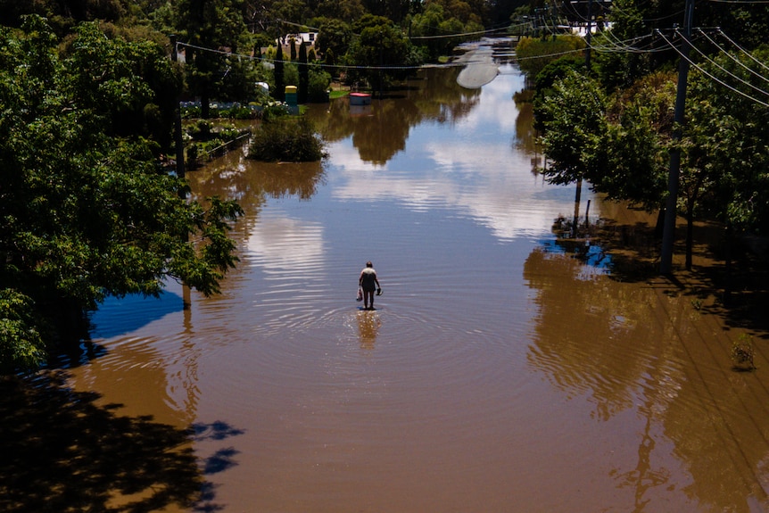A drone shot looking down at a flooded road as a person in the distance walks through the water covering the road