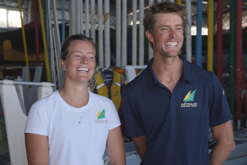 A young man and woman grinning together in the boat shed of a sailing club.