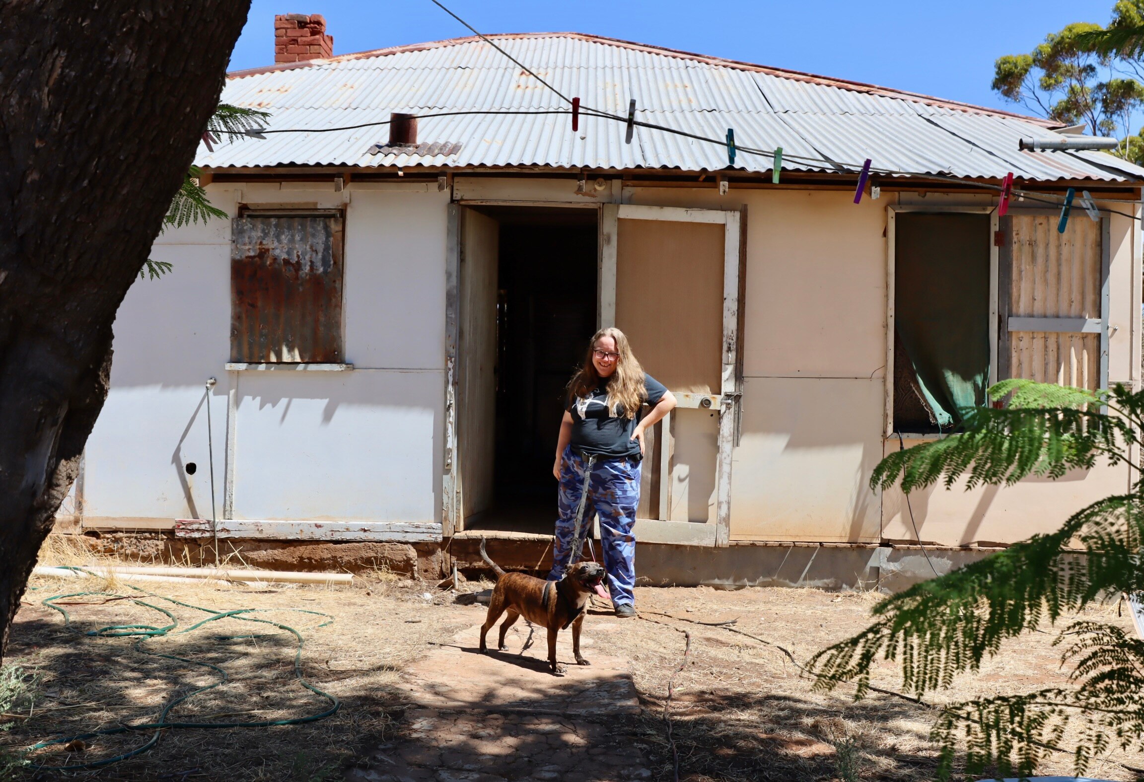old tin house with woman and dog in front of it 