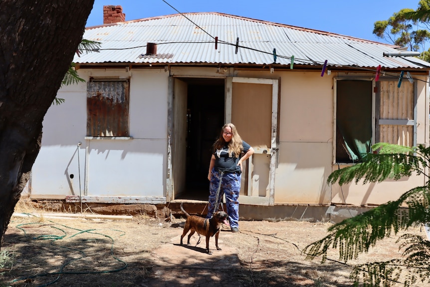 old tin house with woman and dog in front of it 