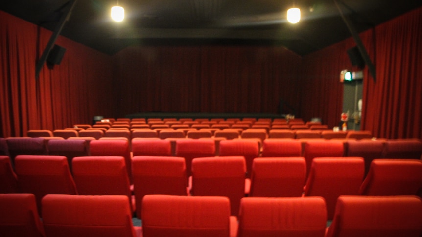 A room full of red padded chairs facing a screen at the front, with red curtains down each side wall.