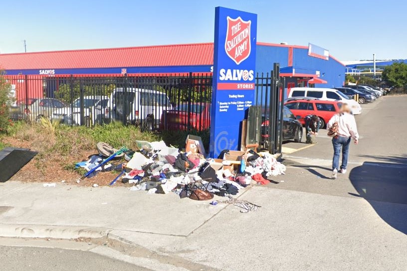 A woman walks past a a Salvos Stores sign with clothes dumped underneath.