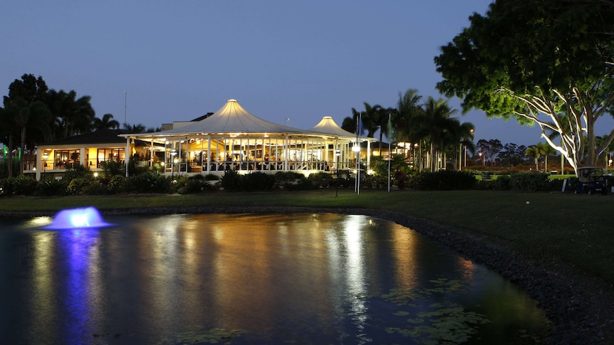 Night time image of lake with a fountain and a sporting clubhouse in the background.