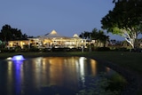 Night time image of lake with a fountain and a sporting clubhouse in the background.