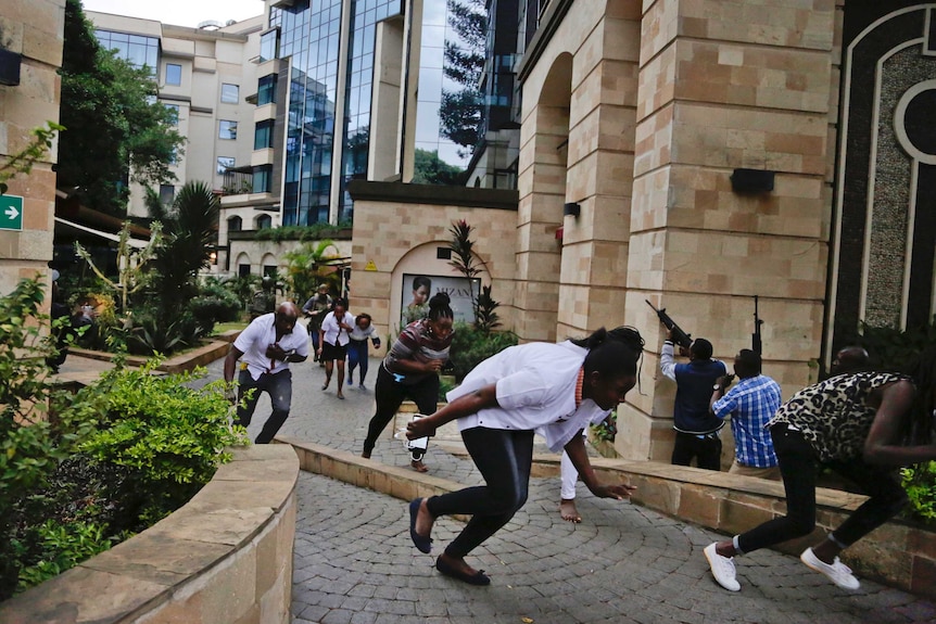 Civilians flee as security forces aim their weapons at the hotel buildings.