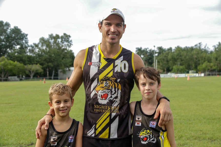Cameron Ilett stands in between his two children at the Nightcliff Football Oval before training.