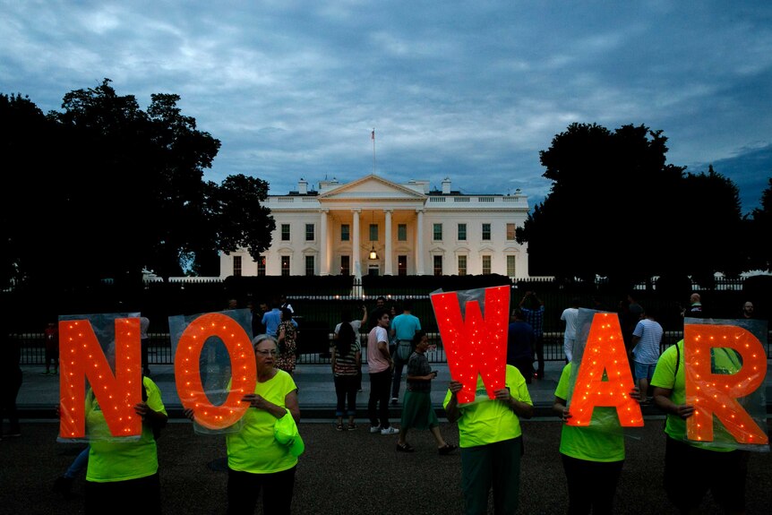 Five protesters in high-viz hold signs spelling out "No War" outside the White House in Washington.