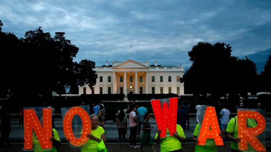 Five protesters in high-viz hold signs spelling out "No War" outside the White House in Washington.