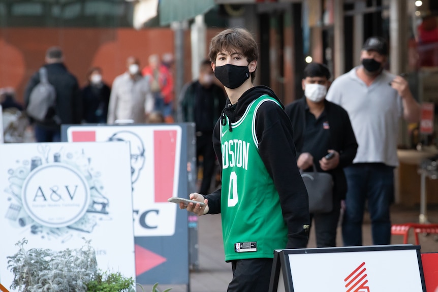 A teenage boy wearing a mask and a bright green basketball jersey in the street