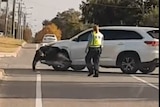 A screenshot showing a white SUV hitting a man with its front-left wheel arch on a suburban street.