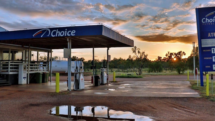 A petrol station in a rural setting - the sun is setting and some water is on the ground.