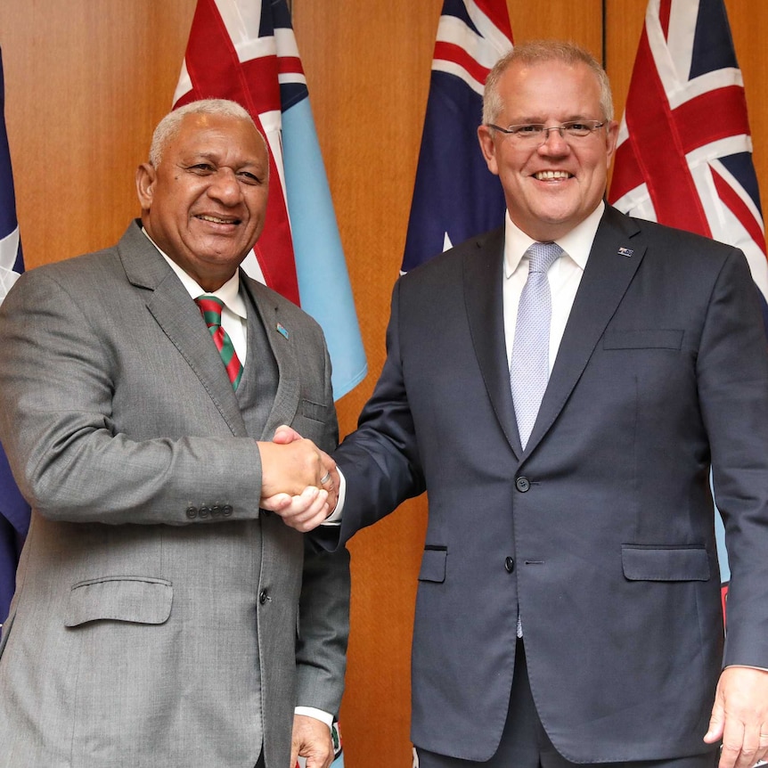 Fiji Prime Minister Frank Bainimarama shakes hands with Australian Prime Minister Scott Morrison in front of national flags.