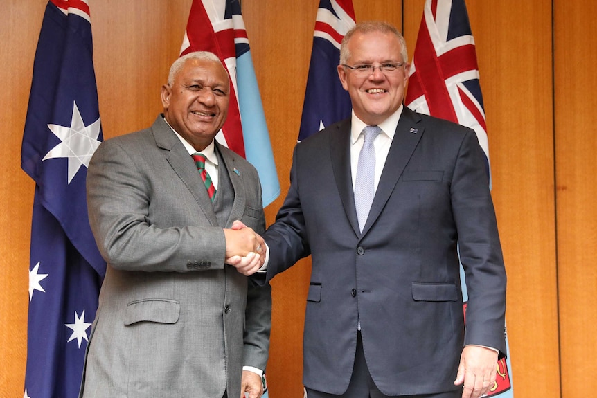 Fiji Prime Minister Frank Bainimarama shakes hands with Australian Prime Minister Scott Morrison in front of national flags.