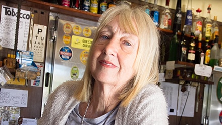 A woman with blond hair leaning on the bar of a pub.
